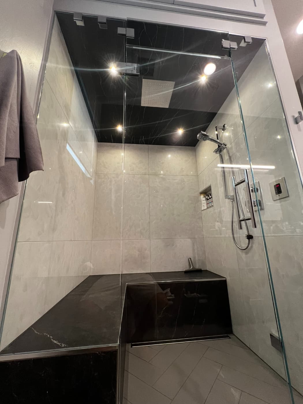 Walk-in glass shower with large white tile and a black stone bench