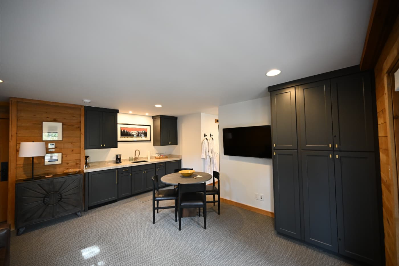 Kitchenette with charcoal cabinets, a wall-mounted TV and a small dining table