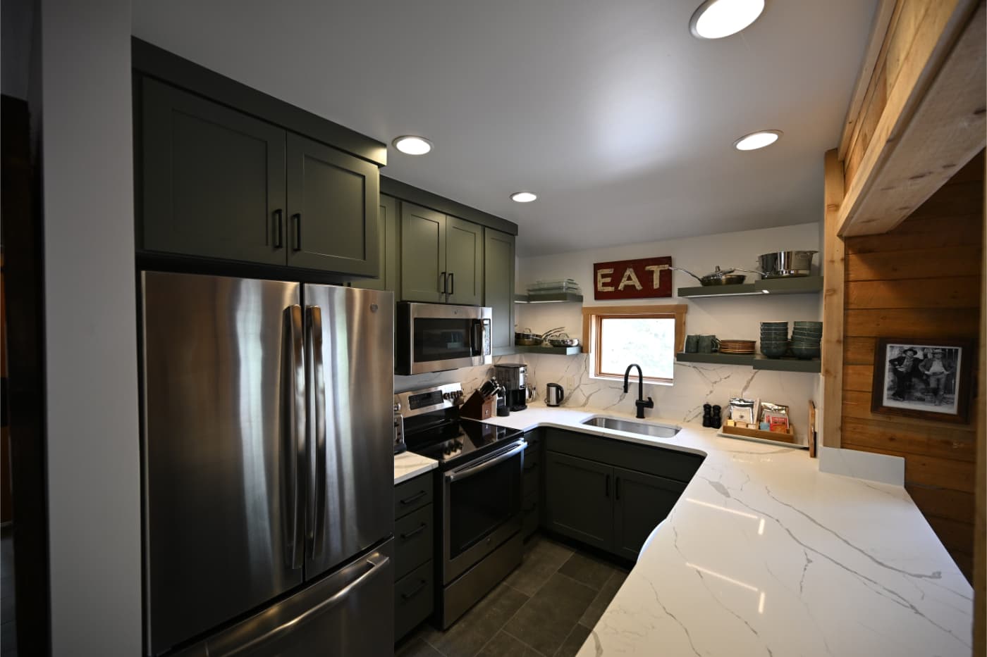 Kitchen with dark green cabinets, white marble-look counters and open shelving