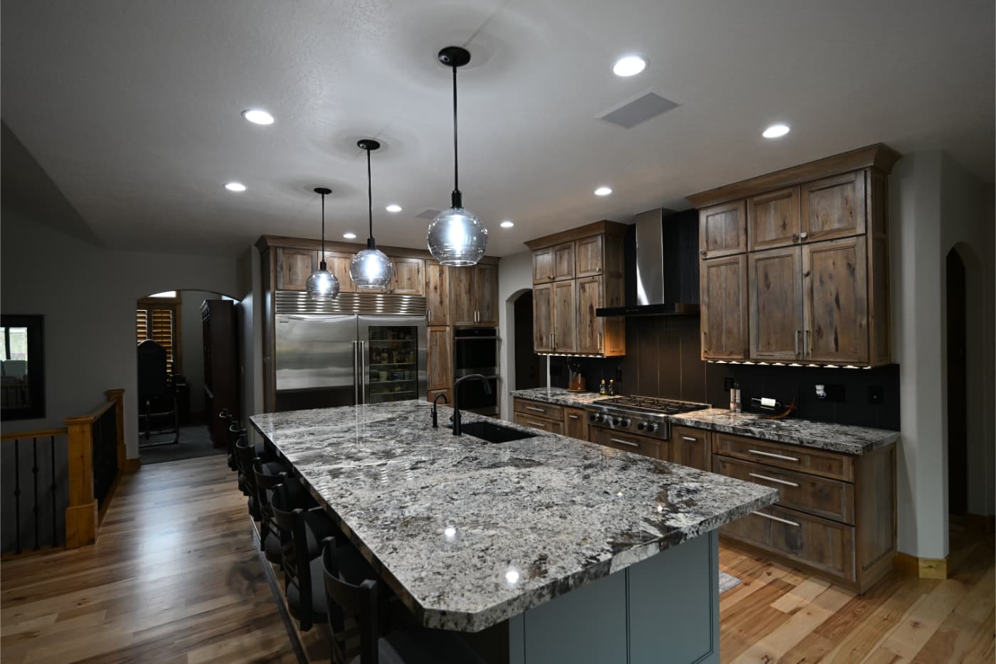 Long granite island with glass pendant lights and rustic wood cabinets