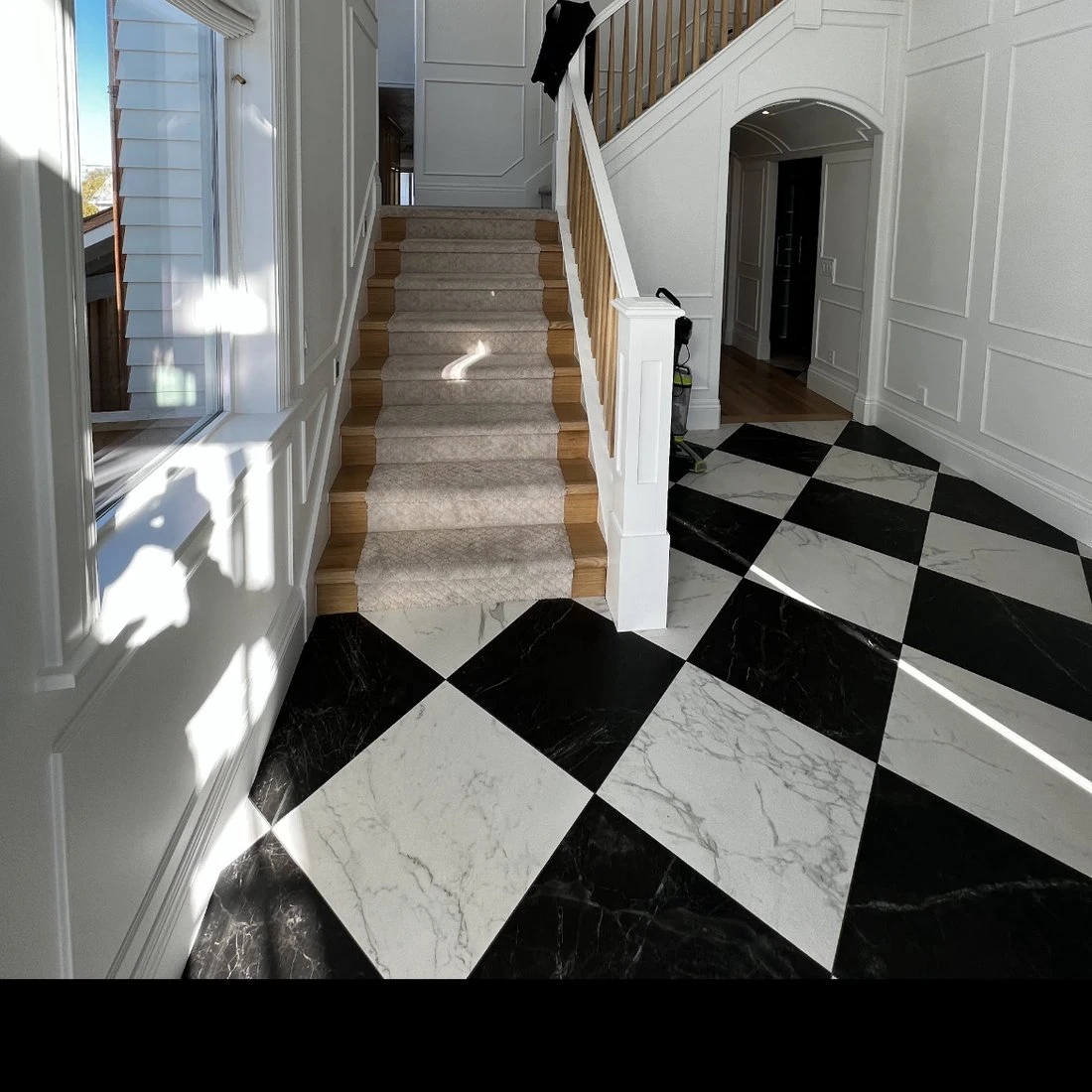 Entryway after: white paneled walls, light oak stairs and checkerboard marble floor