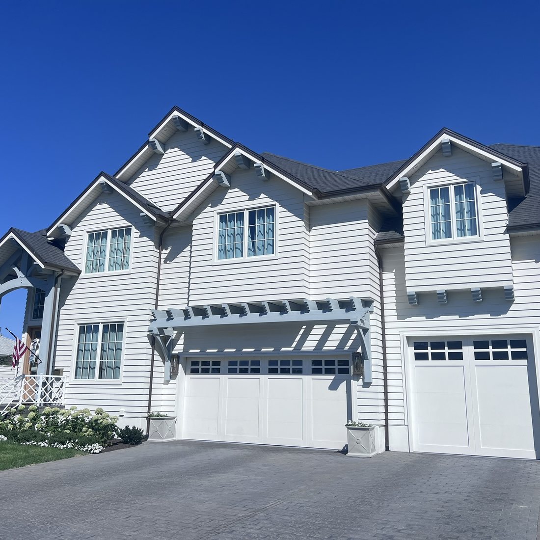 Exterior after: white lap siding, gabled dormers and a pergola over the garage