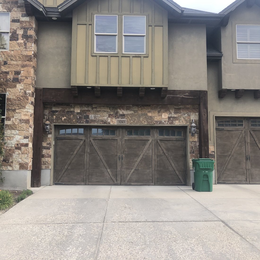Exterior before: tan stucco, stone base and dark wood garage doors