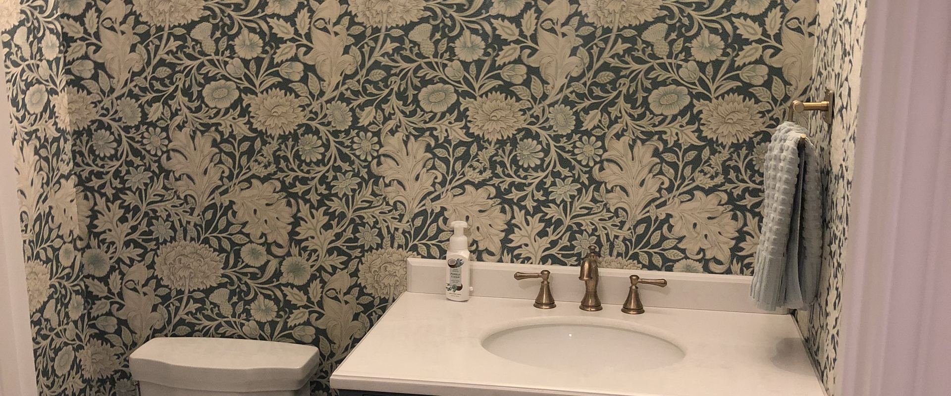 Powder bathroom with patterned wallpaper and a navy vanity