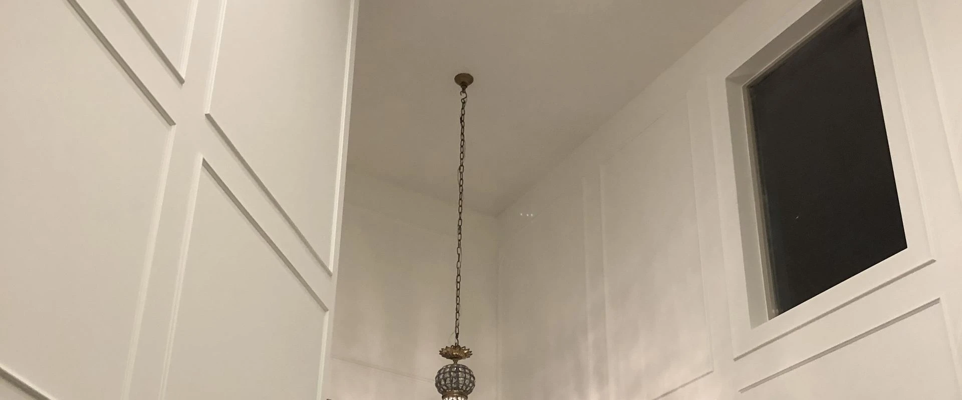 White paneled wall and chandelier in a remodeled entry