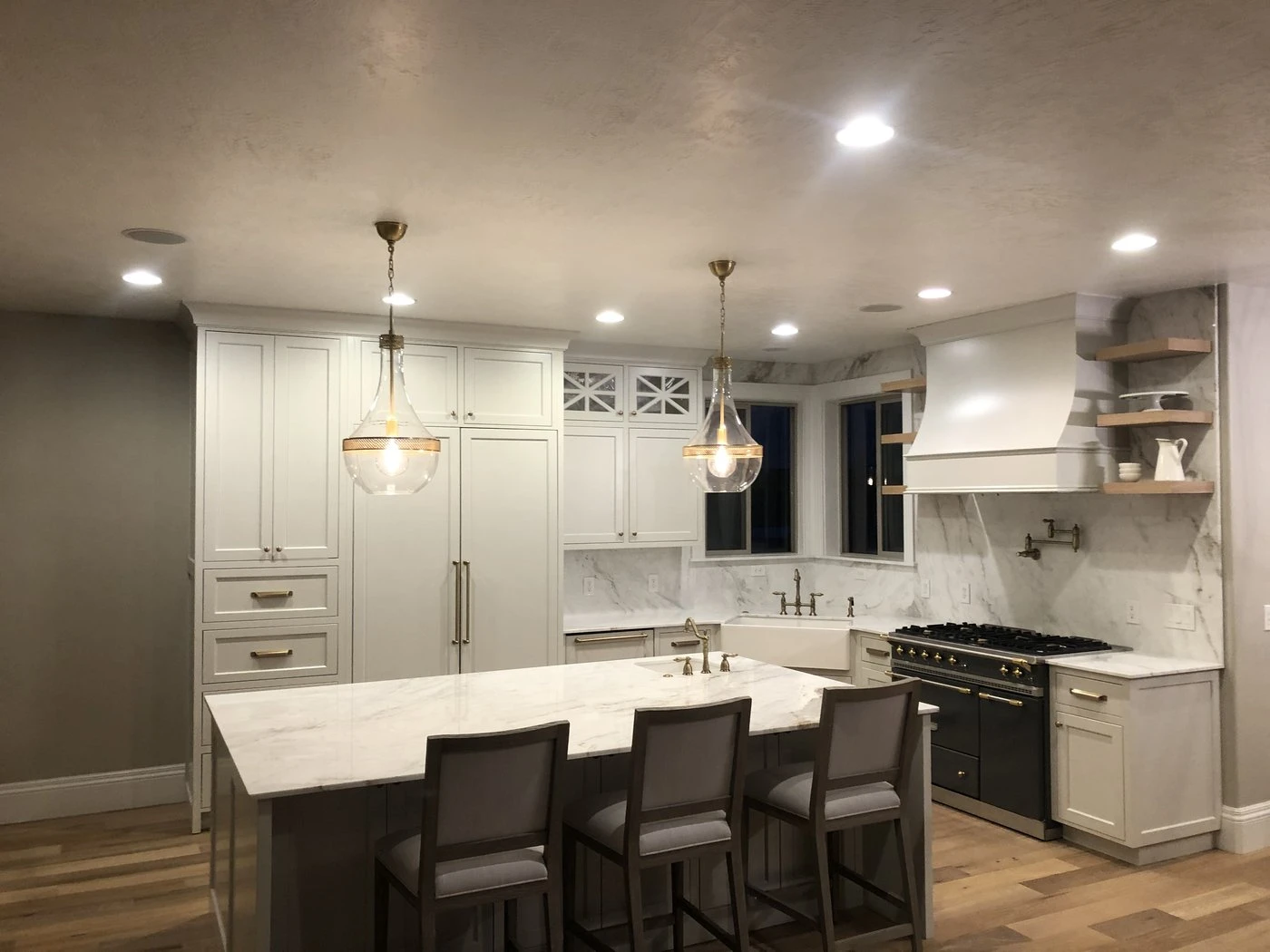 Remodeled kitchen with white cabinetry, marble island, pendant lights and a professional range