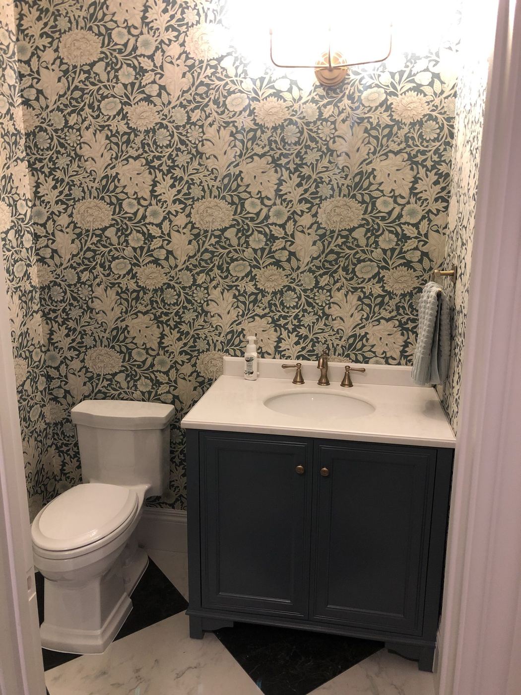 Powder bathroom with patterned wallpaper, a navy vanity and marble floor