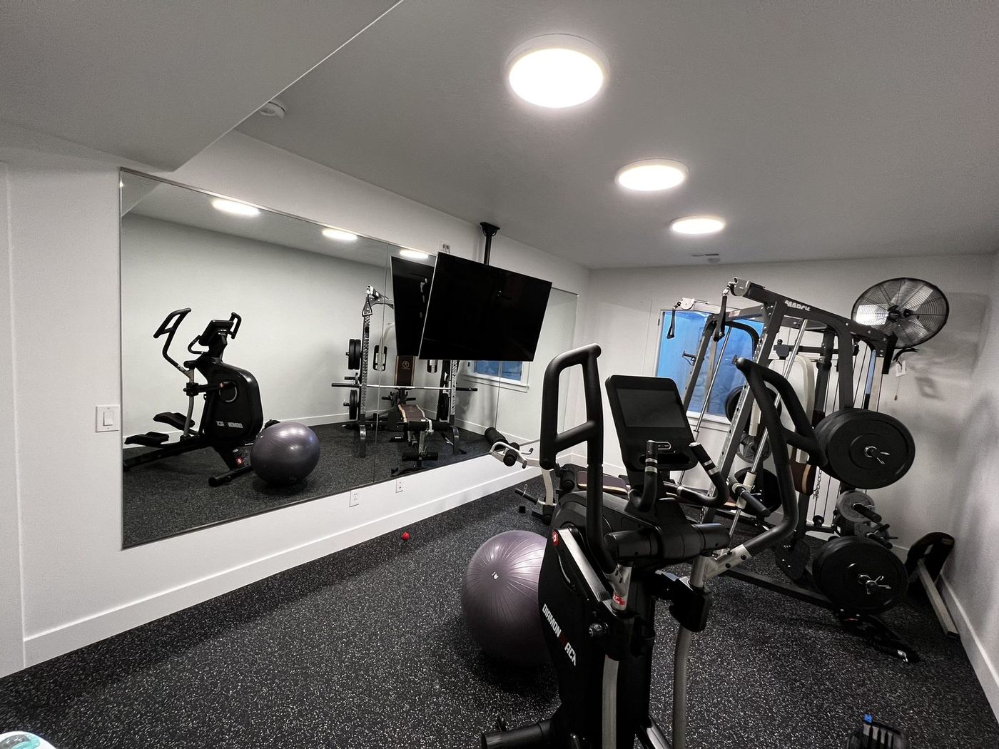 Finished basement home gym with rubber flooring and a mirrored wall
