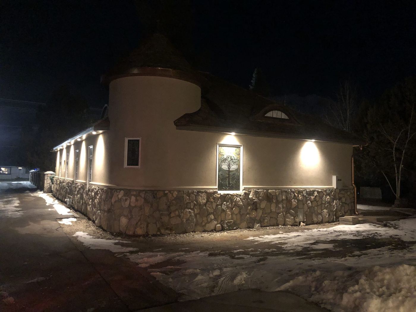 Exterior renovation with a stone base, stucco walls and a turret at night